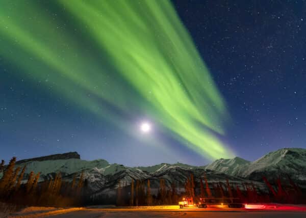 A long haul truck rests at a material site off the Dalton Highway in the Brooks Range as the aurora borealis soars in the sky.